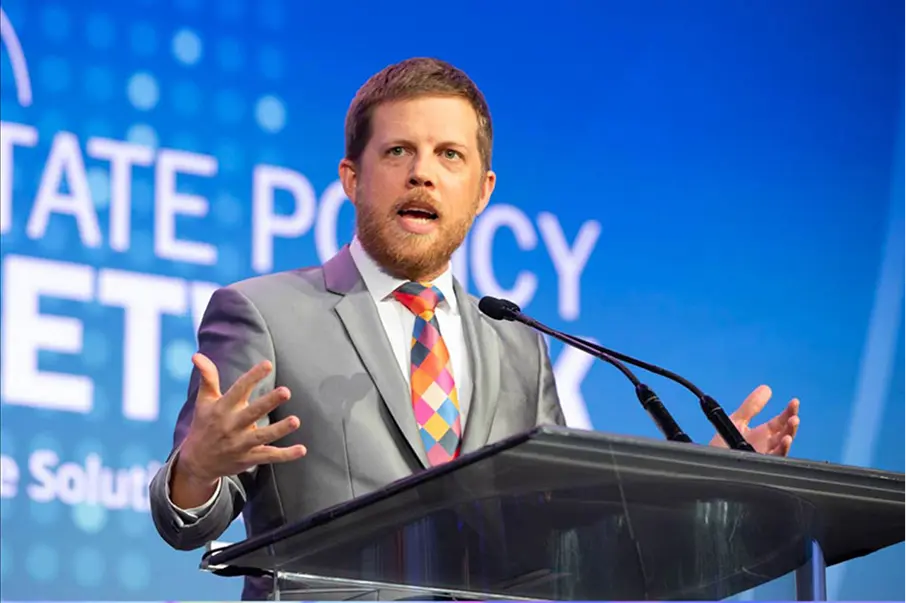 Speaker at a podium with a blue conference backdrop.