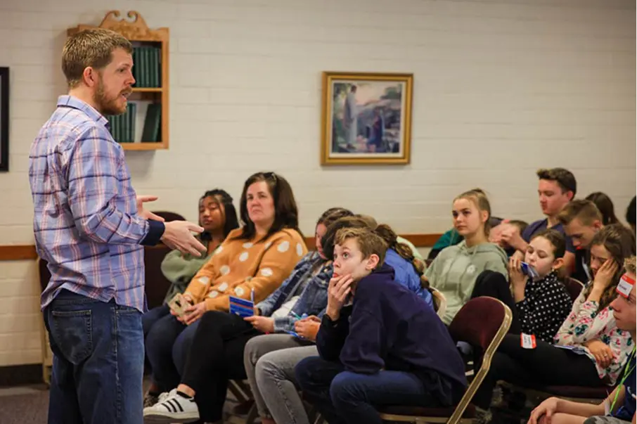 Presenter addressing a small seated group in a classroom setting.